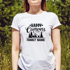 Puede incluir: Camiseta blanca con un dise&ntilde;o gr&aacute;fico negro que dice "Happy Campers" con una silueta de caravana y &aacute;rboles. El texto "FAMILY NAME" est&aacute; debajo del gr&aacute;fico.