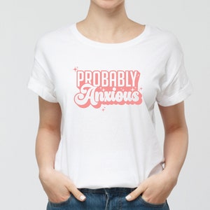 K&ouml;nnte beinhalten: Wei&szlig;es T-Shirt mit dem Text "PROBABLY Anxious" in rosa Retro-Schrift.