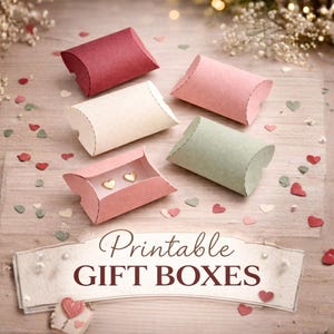 May include: An overhead shot displays five colorful pillow gift boxes, including red, pink, cream, and green. One pink box is open, revealing gold heart-shaped earrings. The words "Printable GIFT BOXES" are printed on a banner below the boxes, with heart-shaped confetti scattered around.