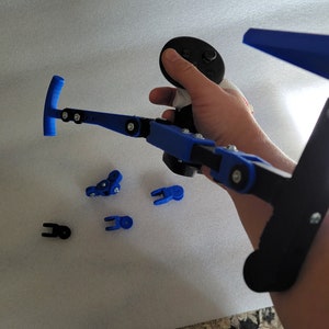 May include: A 3D printed blue and black arm brace with a joystick attached. The brace is designed to help people with disabilities play video games.