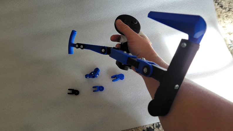 May include: A 3D printed blue and black arm brace with a joystick attached. The brace is designed to help people with disabilities play video games.