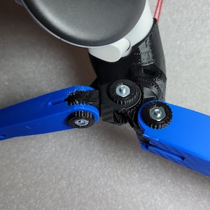 May include: A close-up of a blue 3D printed tripod with black adjustable joints. The tripod is designed to hold a camera or other device.