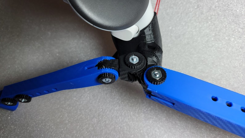 May include: A close-up of a blue 3D printed tripod with black adjustable joints. The tripod is designed to hold a camera or other device.
