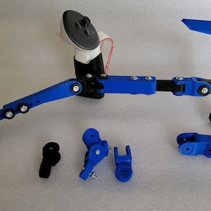 May include: A blue and black 3D printed device with multiple joints and a handle. The device is designed to hold a phone or other device. There are several spare parts for the device, including a blue handle and a blue joint.