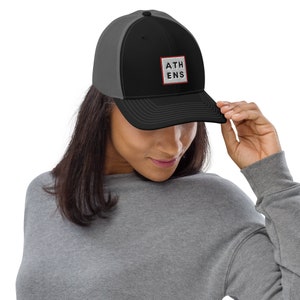 May include: A black and grey trucker hat with a red and white square patch that says "ATHENS" in white letters.