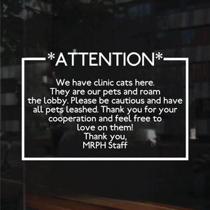 A sign with white text. The text reads: *ATTENTION* We have clinic cats here. They are our pets and roam the lobby. Please be cautious and have all pets leashed. Thank you for your cooperation and feel free to love on them! Thank you.