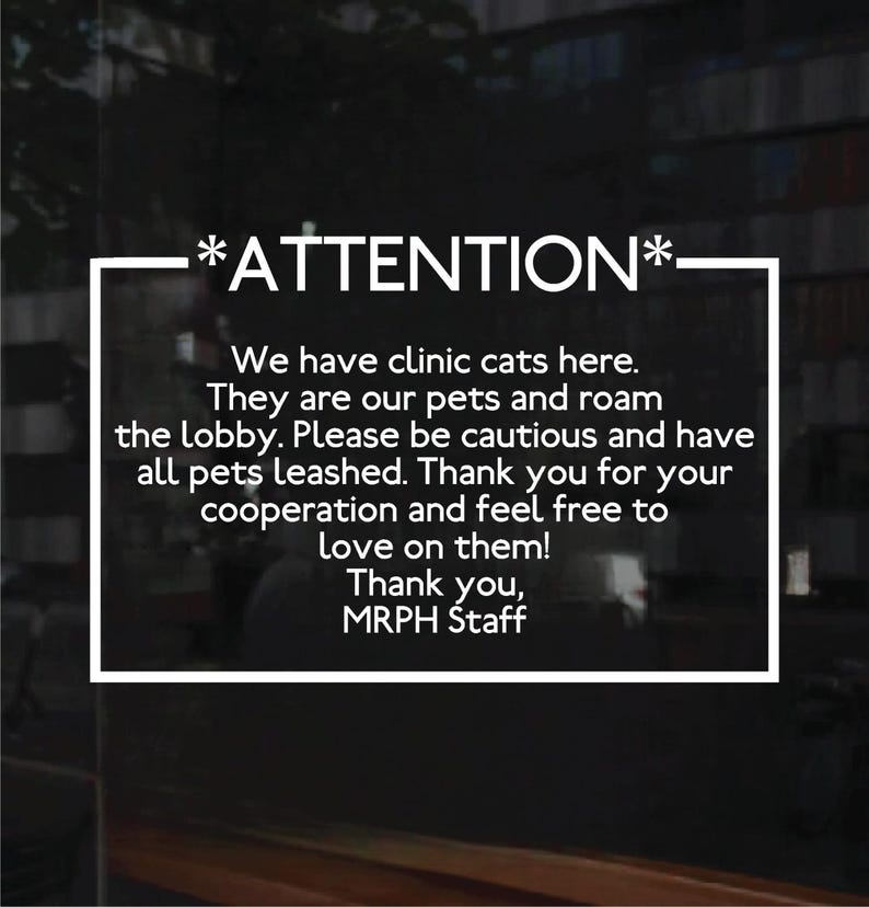 A sign with white text. The text reads: *ATTENTION* We have clinic cats here. They are our pets and roam the lobby. Please be cautious and have all pets leashed. Thank you for your cooperation and feel free to love on them! Thank you.