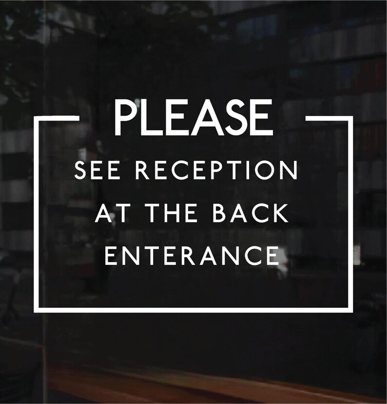 May include: A rectangular sign with a white border on a dark background featuring the white text PLEASE SEE RECEPTION AT THE BACK ENTERANCE. The sign is designed for clear communication and is displayed on a glass surface with a dark, blurred interior.