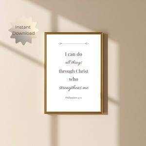 Può includere: Una stampa artistica da parete rettangolare in una sottile cornice dorata con il testo nero I can do all things through Christ who strengthens me Philippians 4:13 centrato su uno sfondo bianco con un piccolo elemento decorativo a linea.