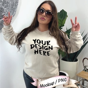 Può includere: Una felpa beige a maniche lunghe con la scritta "YOUR DESIGN HERE" stampata in nero. La felpa è indossata da una persona che indossa pantaloni di pelle neri e occhiali da sole.