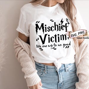 May include: White t-shirt with black text that reads "Mischief Victim. We are up to no good."  The text is in a stylized font and includes a lightning bolt graphic.  The shirt is being worn by a person.