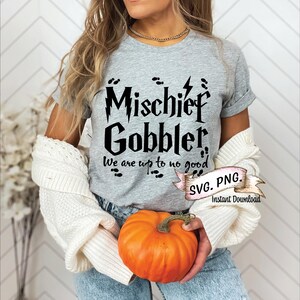 Puede incluir: Una camiseta gris con texto negro que dice "Mischief Gobbler, We are up to no good". El texto está en una fuente estilizada que recuerda a la serie de Harry Potter. La camiseta la lleva puesta una persona que sostiene una calabaza.