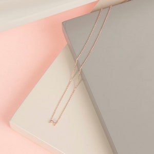 Peut inclure: Un collier délicat en chaîne or rose avec un petit pendentif rectangulaire en pierre précieuse transparente.