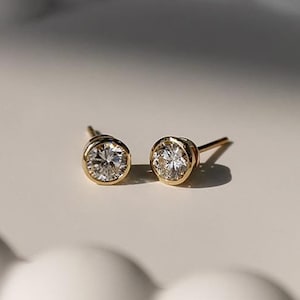 May include: A pair of gold stud earrings with round, clear gemstones.