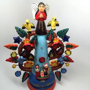 May include: A colorful, hand-painted ceramic Tree of Life sculpture. The tree features an angel at the top, birds, leaves, flowers, and a nativity scene at the base. The base is blue, with brown branches and colorful accents.