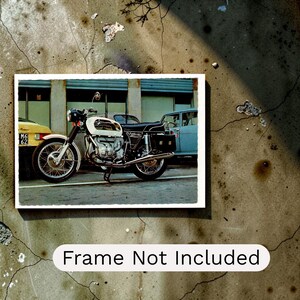 May include: A vintage photograph print featuring a white and black BMW motorcycle parked on a street. The image shows the motorcycle in profile with a yellow car and a light blue car in the background. The text Frame Not Included is printed below.