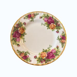 May include: A round white porcelain plate featuring a decorative border of pink, red, and yellow roses with green leaves. The rim of the plate is finished with a thin, scalloped gold trim, providing a distinct edge to the floral pattern design.