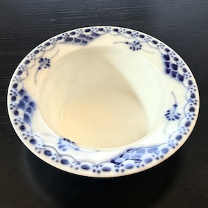 May include: A round white porcelain bowl featuring a wide, flat rim decorated with a delicate blue floral and lace-like pattern. The interior of the bowl is smooth and plain white, while the outer edge displays intricate blue painted details.