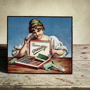 May include: A vintage-style rectangular sign featuring an illustration of a person holding a harmonica. The sign displays an open box of harmonicas with the text Prime quality printed inside. Additional harmonicas and cases are shown on a table.