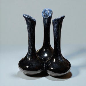 May include: Three black vases with a glossy finish. The vases have a bulbous base and a slender, curved neck. The interior of the neck has a blue and white speckled pattern. The vases are arranged closely together.