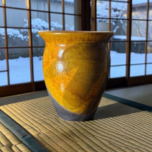 May include: A ceramic vase with a flared rim, featuring a vibrant yellow and orange crackle glaze on the upper portion and a solid dark gray matte finish on the lower base, showcasing a distinct contrast in texture and color throughout.