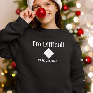 May include: A black sweatshirt with white text that reads "I'm Difficult" and a white diamond symbol. Below the diamond is the text "Park City, Utah".