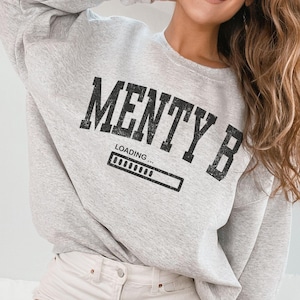 Könnte beinhalten: Grauer Pullover mit dem Text "Menty B" in schwarzen Buchstaben und einem Fortschrittsbalken, der "Loading..." darunter sagt.