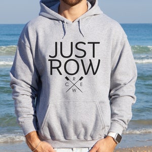 Puede incluir: Sudadera con capucha gris con el texto "JUST ROW" y un logotipo de remos cruzados con la palabra "CREW" en el centro.