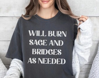 May include: A dark gray t-shirt with the text "Will Burn Sage and Bridges As Needed" printed in white.