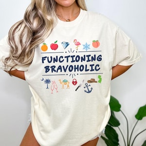 May include: Cream-colored t-shirt with the text "FUNCTIONING BRAVOHOLIC" in navy blue. The shirt features colorful illustrations of various icons, including a diamond, flamingo, and anchor.