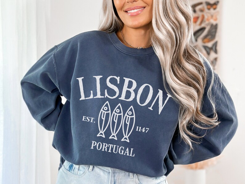 May include: A navy blue sweatshirt with a white graphic design that says "LISBON EST. 1147 PORTUGAL" with three stylized fish below the text.
