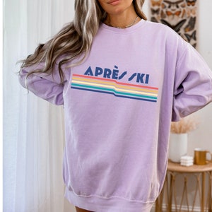 May include: A lavender sweatshirt with a rainbow stripe design and the text "APR&Egrave;S SKI" in navy blue.