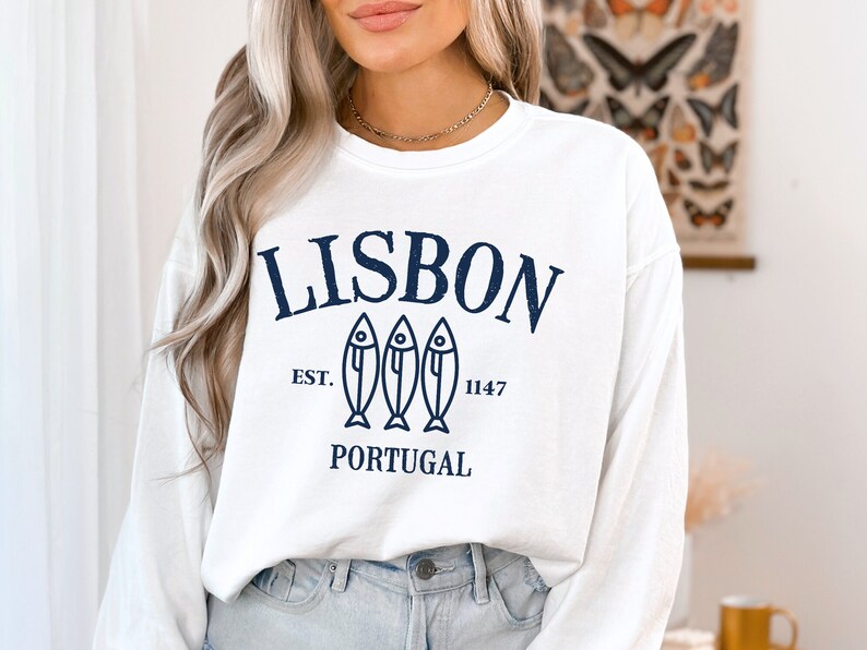 May include: White long-sleeve sweatshirt with a navy blue graphic print that says "LISBON EST. 1147 PORTUGAL" with three stylized fish.