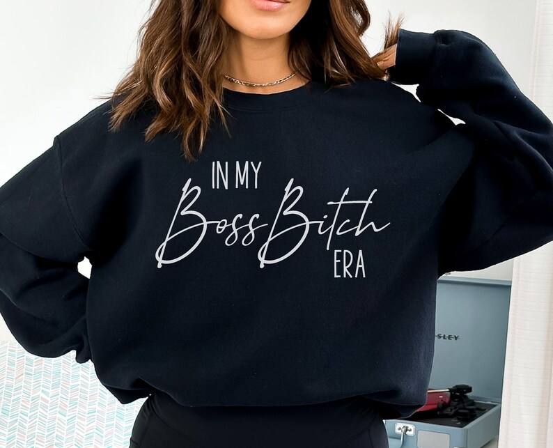 K&ouml;nnte beinhalten: Schwarzer Pullover mit dem Text "In My Boss Bitch Era" in wei&szlig;er Schrift.