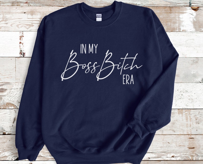 K&ouml;nnte beinhalten: Navyblauer Pullover mit wei&szlig;em Text, der "In My Boss Bitch Era" lautet.