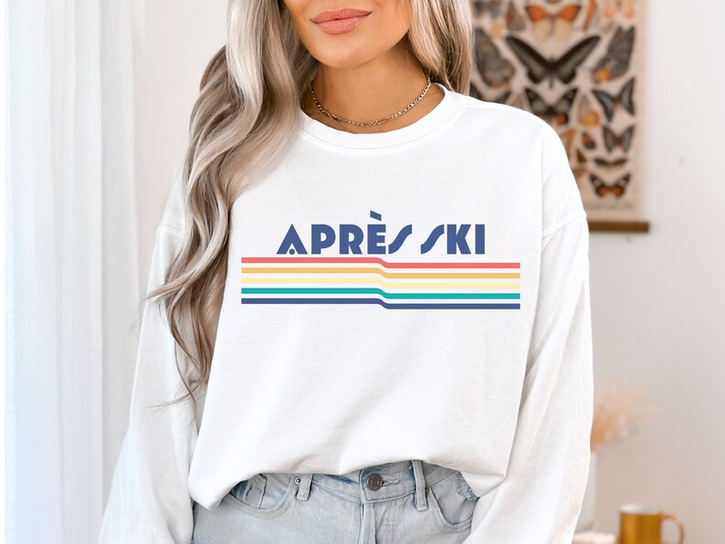 May include: White long-sleeve sweatshirt with a retro rainbow stripe design and the text "APR&Egrave;S SKI" in navy blue.