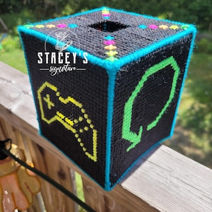May include: Black tissue box cover with neon green and yellow geometric designs. The box has a teal blue trim and colorful accents. The text "STACEY'S signature" is visible on the front of the box. The box is sitting on a wooden surface.