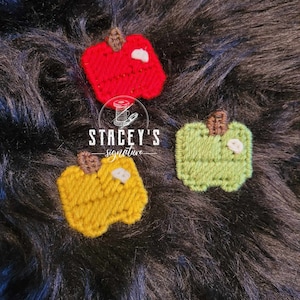 May include: Three felt apple ornaments in red, green, and yellow. The apples have a white stem and a white leaf. The ornaments are on a black fuzzy surface. Stacey's Signature.