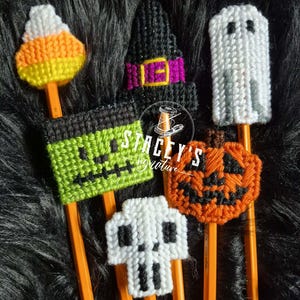 Peut inclure: Un ensemble de cinq embouts de crayon en canevas plastique aux motifs d'Halloween : un bonbon maïs, un chapeau de sorcière noir avec une bande violette, un fantôme blanc, un visage de monstre de Frankenstein vert et une citrouille orange.