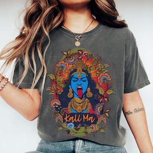 Puede incluir: Una camiseta gris oscuro con un estampado gráfico colorido de Kali Ma, una diosa hindú, rodeada de flores. El texto "Kali Ma" está impreso debajo de la imagen.