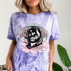 May include: Purple tie-dye t-shirt featuring a graphic of a Pisces zodiac sign. The graphic depicts a black silhouette of a fish with planets and stars inside. The word "Pisces" is written in pink below the fish.