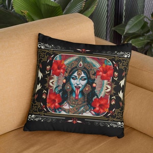 May include: Black throw pillow with a colorful illustration of a Hindu goddess with a red tongue, surrounded by red flowers and gold accents. The pillow has a black background and a gold frame.