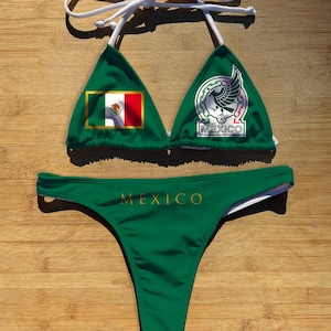 May include: Green bikini set featuring the Mexican flag and the word "MEXICO" in gold lettering. The top has the flag on one cup and a logo on the other. The bottom is a thong style.