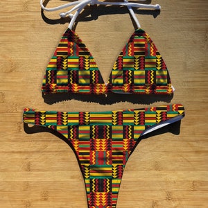 Può includere: Un costume da bagno a due pezzi con un motivo geometrico in tonalità di rosso, giallo, verde e nero. La parte superiore è di stile triangolare con spalline regolabili, e la parte inferiore è di stile a taglio alto.