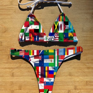 May include: A white bikini with a triangle top and a thong bottom. The fabric is printed with a pattern of flags from around the world.
