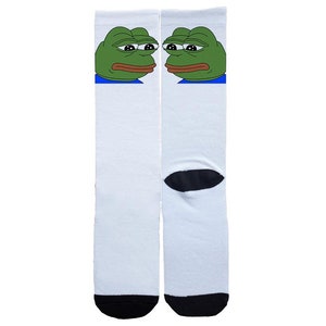 May include: A pair of white socks with a green frog face on each sock. The frog has a sad expression and is wearing a blue shirt.