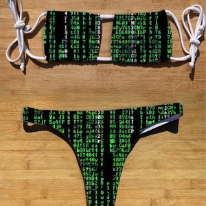 May include: Black and green bikini top and bottom with a computer code pattern. The top has a halter style with adjustable straps. The bottom is a cheeky style with a high leg cut.