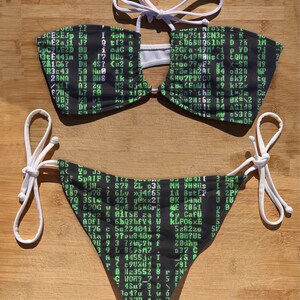 May include: Black and green bikini top and bottom with a white string tie. The fabric has a green computer code pattern.