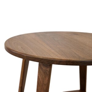 K&ouml;nnte beinhalten: Ein runder Holztisch mit einer braunen Holzplatte und drei Beinen. Der Tisch ist aus massivem Holz gefertigt und hat eine nat&uuml;rliche Oberfl&auml;che.