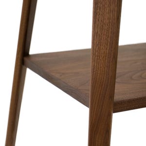 K&ouml;nnte beinhalten: Nahaufnahme eines Holzregals mit dunkelbrauner Oberfl&auml;che. Das Regal ist aus massivem Holz gefertigt und hat ein schlichtes, modernes Design.